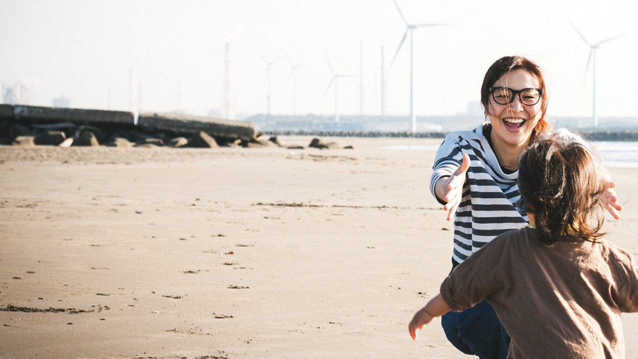 Дете тича при майка си на плаж с вятърни мелници